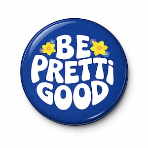 May include: A round, blue button with the words "BE PRETTI GOOD" in white, retro-style lettering. Yellow and purple flower graphics are on the top. The button has a glossy finish and a slight shadow.