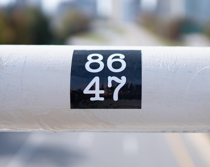 Puede incluir: Un tubo de metal blanco con una pegatina negra que dice "86 47".