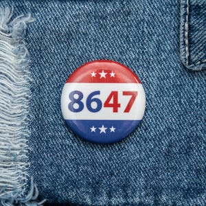 May include: A red, white, and blue button with the number 8647 printed on it. The button is on a blue denim background.