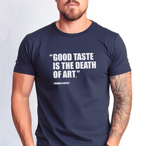 May include: A navy blue t-shirt with white text that reads "GOOD TASTE IS THE DEATH OF ART." - TRUMAN CAPOTE.