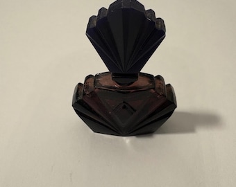 May include: A vintage perfume bottle with a dark purple, Art Deco design. The bottle has a fan-shaped stopper and a geometric, faceted body. The glass is a deep, translucent purple color.