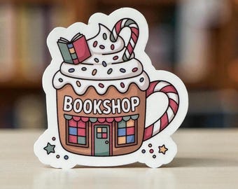 May include: A whimsical sticker featuring a cartoon-style mug labeled "BOOKSHOP." The mug is decorated to resemble a hot beverage with whipped cream, sprinkles, and a candy cane. A small open book sits atop the whipped cream. The mug has a striped handle.