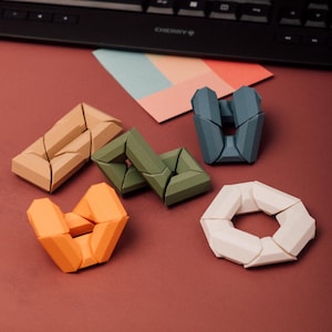 Può includere: Una collezione di puzzle geometrici in legno colorati, nei toni del beige, verde, arancione, blu e bianco. I puzzle sono disposti su una superficie marrone, con una tastiera e un campione di colore sullo sfondo.