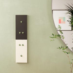 Könnte beinhalten: Eine vertikale Wandgarderobe im zweifarbigen Design mit einem dunkelgrauen oberen Teil und einem cremefarbenen unteren Teil. Die Garderobe verfügt über sechs kleine, runde, metallisch grüne Haken, die paarweise und einzeln angeordnet sind.