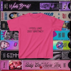 Può includere: Una maglietta rosa acceso con la scritta nera "I FEEL LIKE 2007 BRITNEY". La maglietta è esposta su uno sfondo di vecchie videocassette VHS, molte con Britney Spears.
