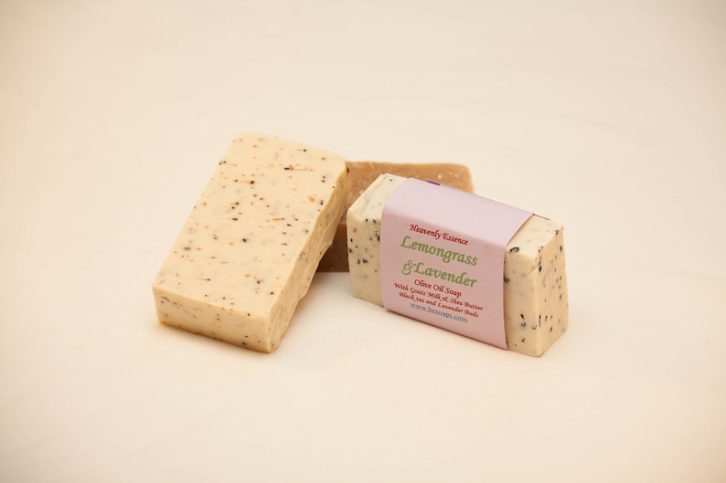May include: Three bars of handmade olive oil soap. Two bars are plain and one bar is labeled "Heavenly Essence Lemongrass & Lavender Olive Oil Soap" with the text "Rich Goats Milk, Shea Butter, Black Tea and Lavender Buds" and a website address.