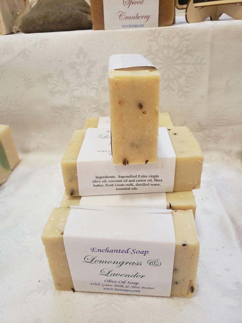 May include: A stack of handmade soap bars with a white label that reads "Enchanted Soap Lemongrass & Lavender Olive Oil Soap with Goats Milk & Shea Butter www.hesoaps.com".