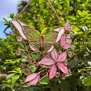 May include: Stained glass butterfly and flower suncatcher. The butterfly has white and green wings, with a copper frame. Pink flowers and green leaves are also included in the design. The text "GrapeseedCraft" is visible on the image.