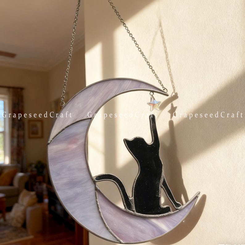 May include: A stained glass crescent moon with a black cat silhouette reaching for a star. The moon is lavender and white, with a silver chain for hanging. The text "GrapeseedCraft" is visible.