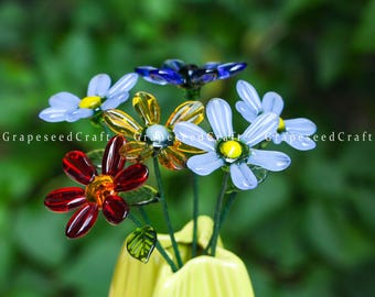 May include: A bouquet of glass flowers in a yellow vase. The flowers are various colors, including blue, red, and yellow. The text "GrapeseedCraft" is visible on the image.