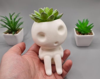 May include: White ceramic planter shaped like a person with a small succulent plant in the head. The planter has two small eyes and a mouth.