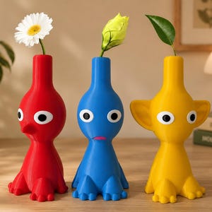 Peut inclure: Trois vases en forme de personnages de couleur rouge, bleue et jaune. Chaque vase présente une finition mate lisse, de grands yeux blancs avec des pupilles noires et un goulot étroit. Une marguerite blanche, un bouton floral et une feuille verte.