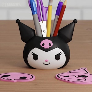 May include: A black and white Kuromi-themed desk organizer with a pink skull emblem, holding pens, pencils, and scissors. Two pink Kuromi-shaped coasters are on the wooden surface. The organizer has a smiling face design.
