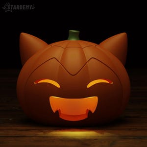 May include: An orange pumpkin-shaped lamp with cat ears and a carved, glowing face featuring closed eyes and a wide, toothy grin. The top of the pumpkin has a small green stem, and the word STARDEMY is printed in the upper left corner.