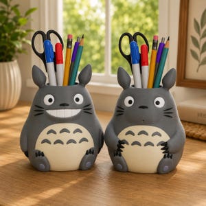 Peut inclure: Deux porte-crayons gris en forme de créatures de dessin animé avec des ventres couleur crème et des marques sombres. Chaque porte-crayon contient une paire de ciseaux noirs, un marqueur bleu, un marqueur rouge, un crayon jaune, un stylo violet et un crayon sarcelle.