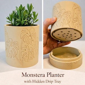 May include: A cylindrical beige planter featuring an embossed monstera leaf pattern on the exterior. The planter includes a detachable base with a hidden drip tray and a perforated bottom for drainage, shown holding a green plant.
