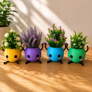 Op de afbeelding: Vier ronde plantenbakken met zwarte, stokachtige armen en benen, elk met een gezicht met zwarte ogen en roze wangen. De potten zijn geel, paars, blauw en groen en bevatten kunstplanten met witte, paarse en roze bloemen.
