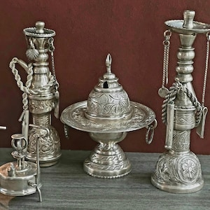 May include: A set of four silver-plated decorative objects, including a small burner, a water pitcher, a censer, and a hookah. The objects are intricately decorated with floral patterns and have a traditional Middle Eastern design.