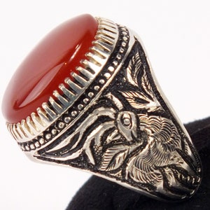 May include: A silver ring with an oval, reddish-brown stone. The ring has intricate floral and leaf patterns on the band. The stone is set in a detailed bezel.