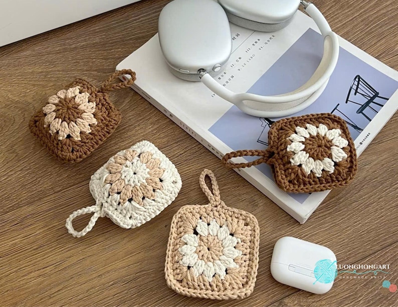 Puede incluir: Tres fundas cuadradas de ganchillo para auriculares inal&aacute;mbricos, cada una con un motivo floral central. Una funda es marr&oacute;n oscuro con centro crema, otra es crema con centro beige y otra es beige con centro crema. Cada funda incluye una peque&ntilde;a asa.