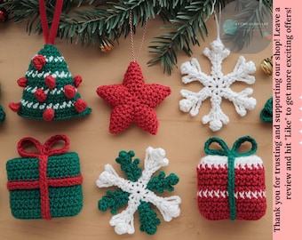 Könnte beinhalten: Eine Sammlung handgefertigter gehäkelter Weihnachtsschmuckstücke. Die Ornamente umfassen einen grünen Weihnachtsbaum, einen roten Stern, weiße und grüne Schneeflocken sowie Geschenkboxen in Rot und Grün. Auf einer Holzoberfläche präsentiert.