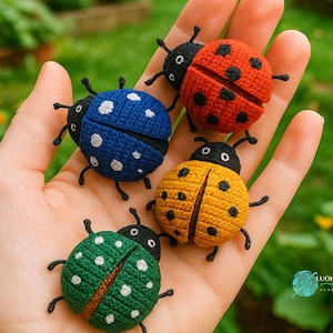 Op de afbeelding: Een hand houdt vier gehaakte lieveheersbeestjes in rood, blauw, geel en groen vast. Elk lieveheersbeestje heeft een zwarte kop en poten, met witte stippen op de blauwe en groene. De lieveheersbeestjes zijn handgemaakt en gedetailleerd.