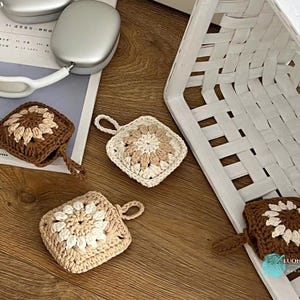Puede incluir: Cuatro fundas cuadradas de ganchillo para auriculares inal&aacute;mbricos, con un motivo floral central en hilo crema y marr&oacute;n. Dos fundas son de color marr&oacute;n oscuro con centro crema, y dos son crema con centro marr&oacute;n claro, cada una con una peque&ntilde;a asa.