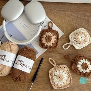 Puede incluir: Tres ovillos de hilo Line Narrate en crema, beige y marr&oacute;n, un ganchillo negro, auriculares plateados y cuatro posavasos cuadrados de ganchillo con un patr&oacute;n de flores en colores a juego y peque&ntilde;as asas para colgar.