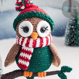 May include: A crocheted owl wearing a red and white striped scarf and a green and red Santa hat. The owl is sitting on a branch with a snowy background.