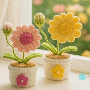 Può includere: Due composizioni floreali all'uncinetto in vasi bianchi. Uno ha un fiore rosa con un centro rosa e un bocciolo, l'altro ha un fiore giallo. I vasi hanno accenti floreali. I fiori hanno steli e foglie verdi.