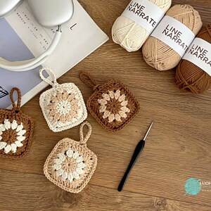 Puede incluir: Cuatro adornos cuadrados de ganchillo con un motivo floral central en tonos crema, beige y marr&oacute;n. Cada adorno tiene un peque&ntilde;o lazo para colgar. Se incluyen tres ovillos de hilo Line Narrate en colores a juego y un ganchillo negro.