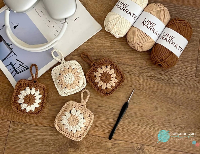 Puede incluir: Cuatro adornos cuadrados de ganchillo con un motivo floral central en tonos crema, beige y marr&oacute;n. Cada adorno tiene un peque&ntilde;o lazo para colgar. Se incluyen tres ovillos de hilo Line Narrate en colores a juego y un ganchillo negro.