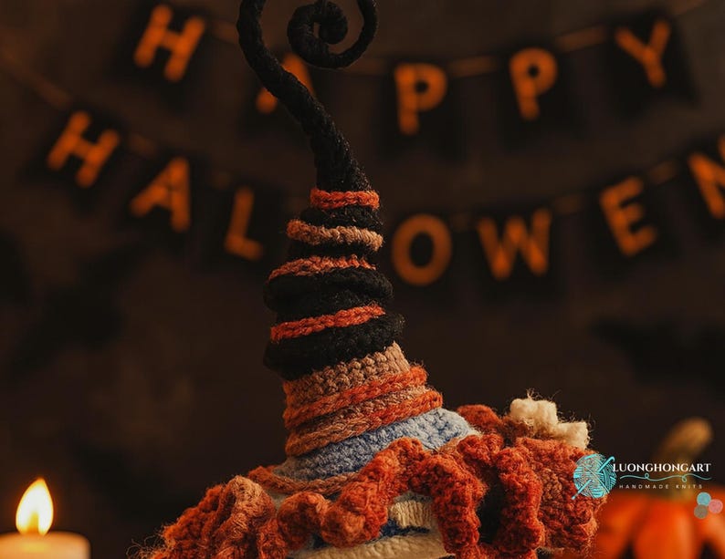 May include: A handmade crochet witch hat in black, orange, and blue, with a curly top. The hat is decorated with orange and brown yarn. The background includes a "HAPPY HALLOWEEN" banner and a lit candle.