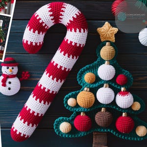 May include: Crocheted Christmas decorations including a candy cane, a Christmas tree, and two snowmen. The candy cane is red and white, the Christmas tree is green with red, white, brown, and gold ornaments, and the snowmen are white with black eyes and buttons, red scarves, and black hats.