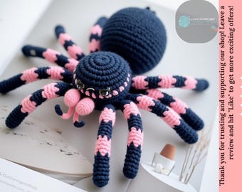 May include: A crocheted spider toy with a black body and pink legs. The spider has large, black eyes and a pink mouth.
