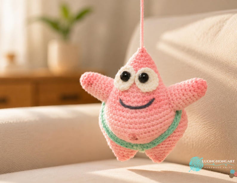 May include: A pink crochet starfish toy with a pointed top, two arms, and two legs. It features large black plastic eyes with white felt backing, a stitched dark blue smile, and a light green waistband. A pink yarn string is attached to the top.
