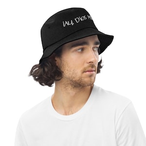 Op de afbeelding: Een zwarte bucket hat met de tekst "¡Ay Dios Mío!" geborduurd in wit op de voorkant.