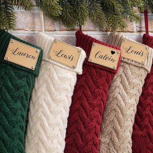 Puede incluir: Cinco calcetines navide&ntilde;os de punto trenzado en verde, crema, rojo, beige y burdeos, cada uno con una etiqueta de madera con un nombre. Nombres: Lauren, Lewis, Calvin, Louis y Selena. Decoraci&oacute;n festiva.