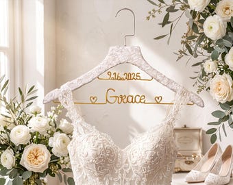 May include: A white lace-covered clothes hanger featuring gold wire lettering that reads "Grace" flanked by two small hearts, with the date "9.16.2025" in gold wire above it, holding a white lace dress with a sweetheart neckline.