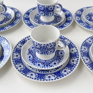 May include: A set of six blue and white teacups and saucers with a floral pattern. The cups and saucers are arranged in a circle on a white surface.