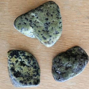 Puede incluir: Tres piedras lisas con manchas verdes y negras. Las piedras tienen una forma irregular y un acabado natural y pulido.