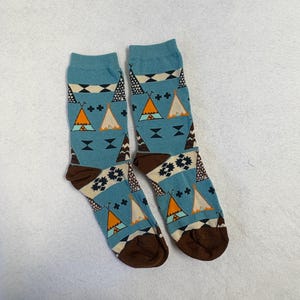 May include: A pair of blue socks with a Native American teepee pattern. The socks have brown heels and toes, and the pattern includes orange, white, and black geometric shapes. The socks are made of a soft, comfortable material.