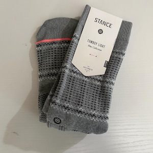 May include: A pair of gray socks with a geometric pattern and a neon pink stripe at the top. The socks are labeled "Tomboy Light Blue Collection" by Stance. The Uncommon Thread logo is also visible.
