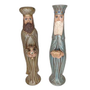 Może przedstawiać: Dwie wysokie, smukłe figurki przedstawiające postacie z brodami, ubrane w długie szaty i nakrycia głowy. Lewa figurka jest beżowa, ma turban i trzyma małe naczynie. Prawa figurka jest niebiesko-szara, ma koronę i trzyma w dłoniach małe pudełko.