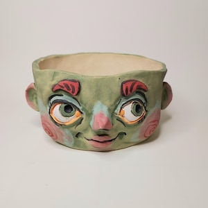 May include: A white ceramic mug with a black handle and the text "But First, Coffee" in a bold, black font. The mug is set against a blurred background, suggesting a cozy setting.