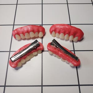May include: Four sets of fake teeth with a pink gum line and a silver clip on the back. The teeth are white and slightly yellowed.