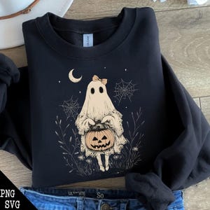 May include: A black sweatshirt featuring a white ghost holding a jack-o'-lantern. The ghost is wearing a pink bow and is surrounded by spiderwebs and stars. The text "Trick or Treat" is printed on the sweatshirt.