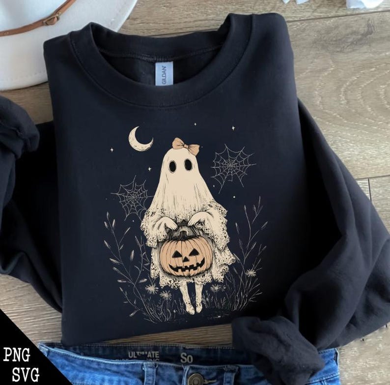 May include: A black sweatshirt featuring a white ghost holding a jack-o'-lantern. The ghost is wearing a pink bow and is surrounded by spiderwebs and stars. The text "Trick or Treat" is printed on the sweatshirt.