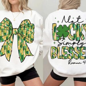 Puede incluir: Sudadera blanca con un gran diseño de lazo verde y dorado en la parte delantera. La parte trasera de la sudadera presenta el texto "Not Lucky Simply Blessed" con un trébol y el versículo bíblico Romanos 4:7-8.