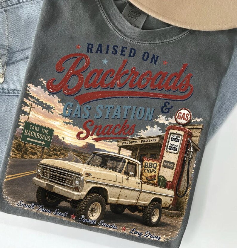 May include: Gray t-shirt with a vintage graphic featuring a cream-colored pickup truck at a gas station. The text reads "RAISED ON Backroads GAS STATION & Snacks". Additional text includes "Take the Backroads", "Small Town Soul", and "Sweet Snacks".